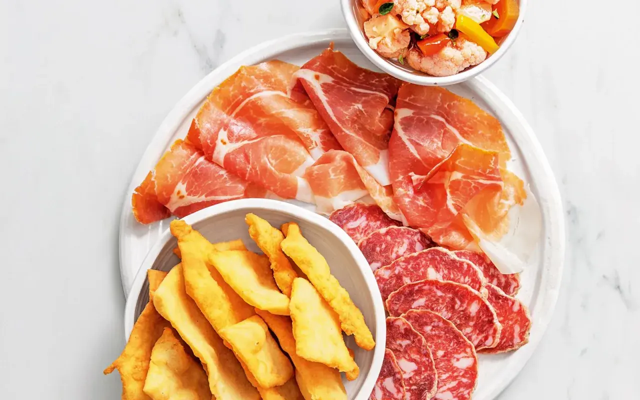 En tallrik med italienska delikatesser: tunt skivad prosciutto, salami och krispiga gnocco fritto. En skål med marinerade grönsaker.