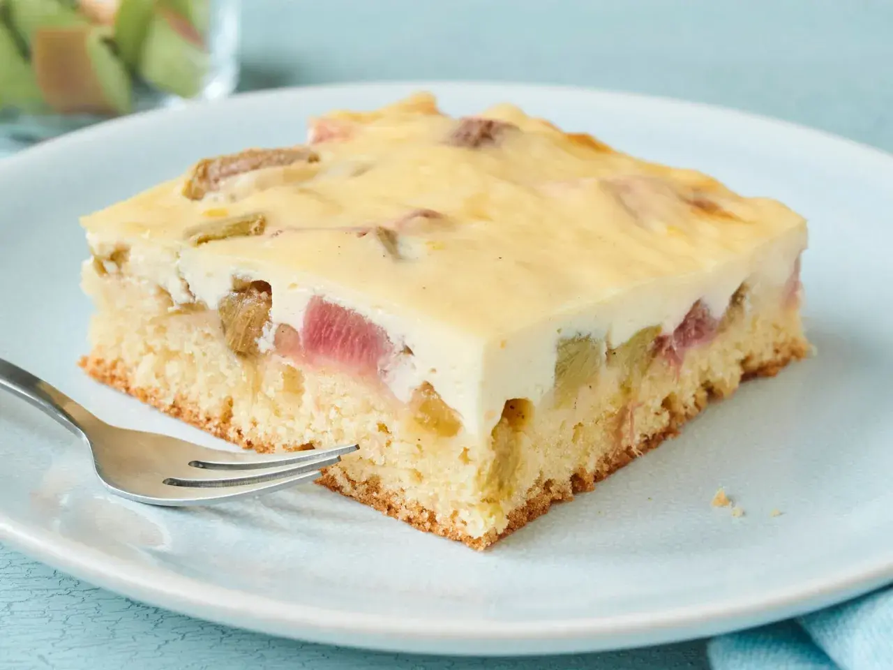Ein Stück Rhabarberkuchen vom Blech mit Vanillepudding und Schmand.