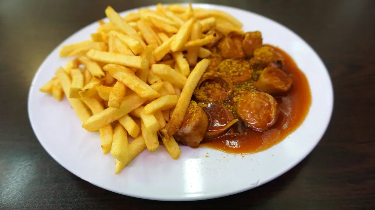 Eine Portion knuspriger Pommes Frites neben einer Currywurst in würziger Sauce, ein Klassiker aus Berlin.