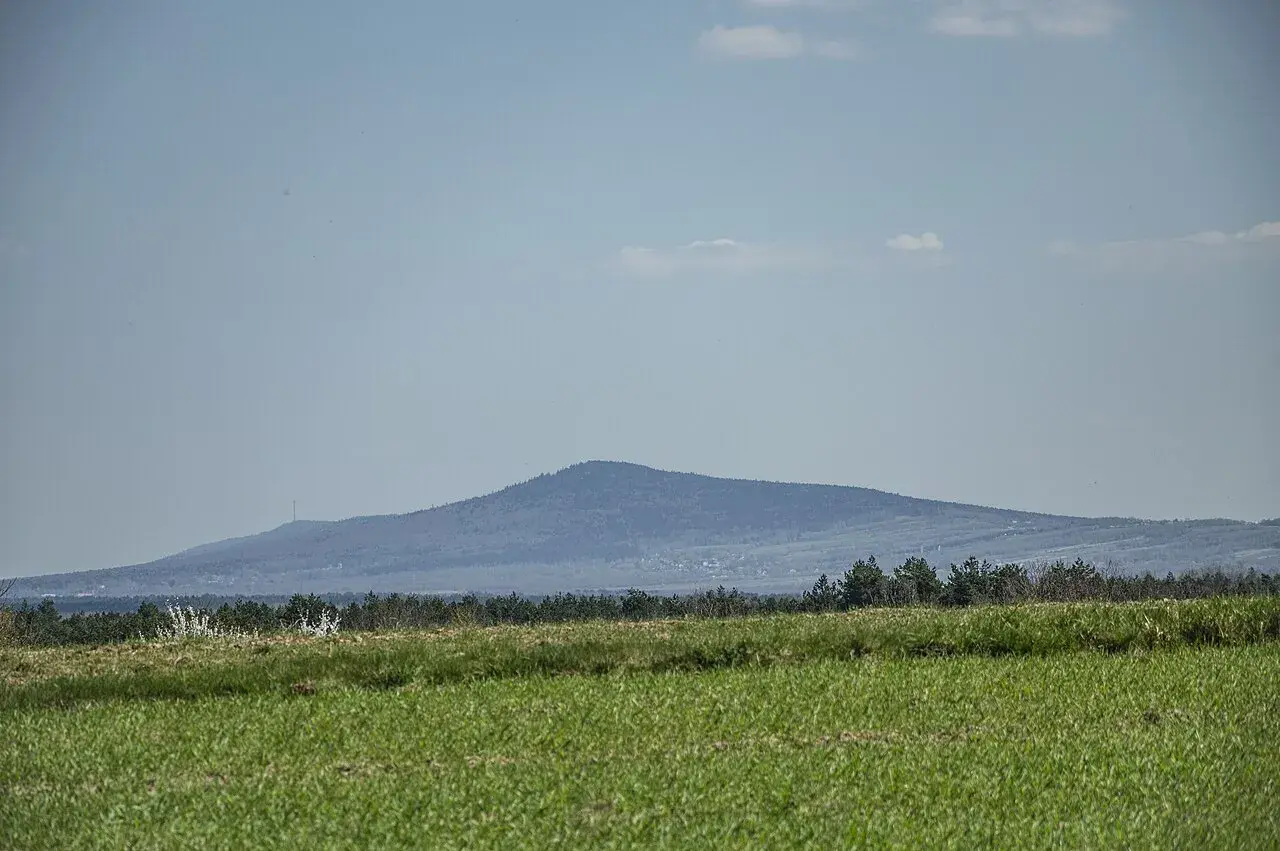 Łagodne, zalesione góry świętokrzyskie szczyty na horyzoncie, z zieloną łąką na pierwszym planie.