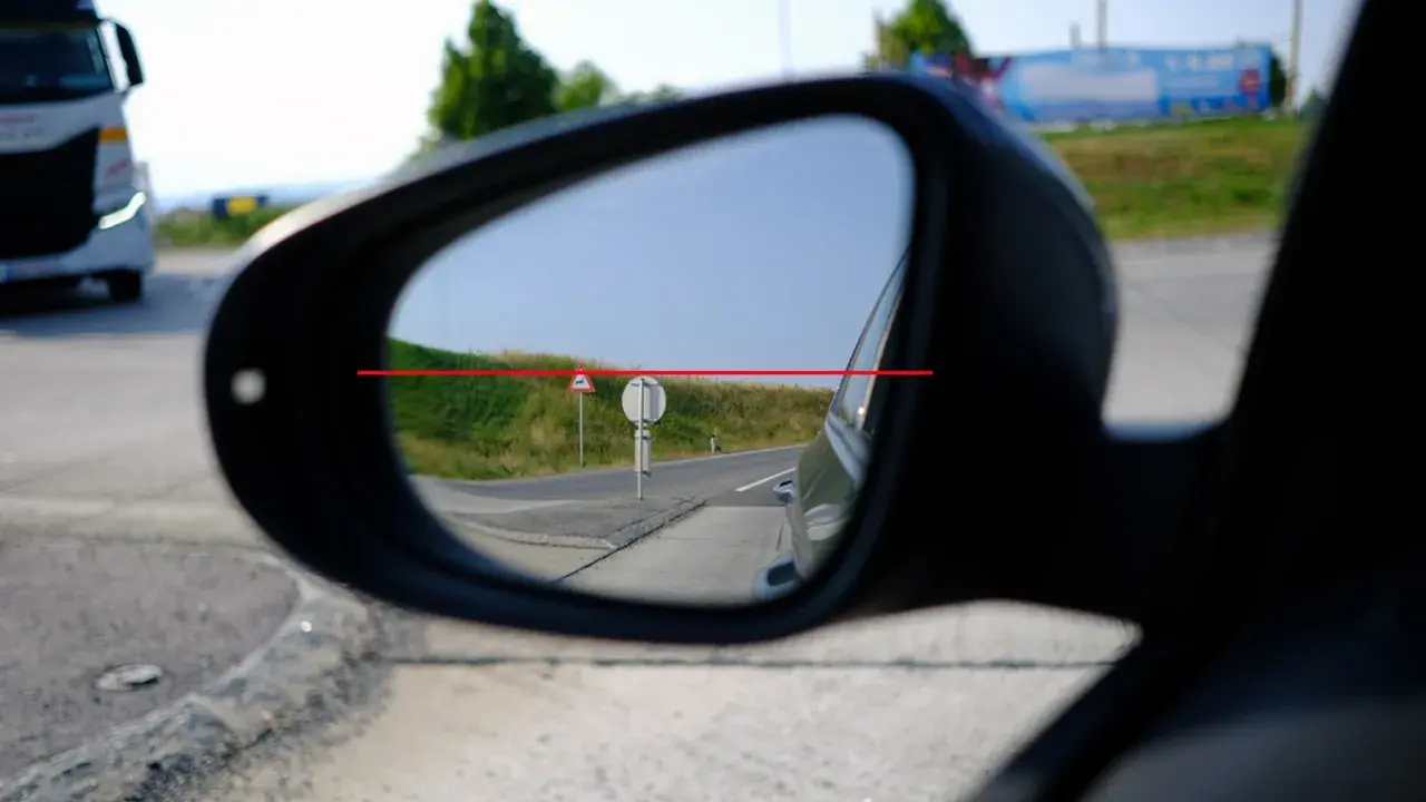 Blick in den Rückspiegel: Ein LKW fährt vorbei. Die rote Linie zeigt, wie man das Spiegelglas richtig einstellen kann, um die Straße im Blick zu behalten.