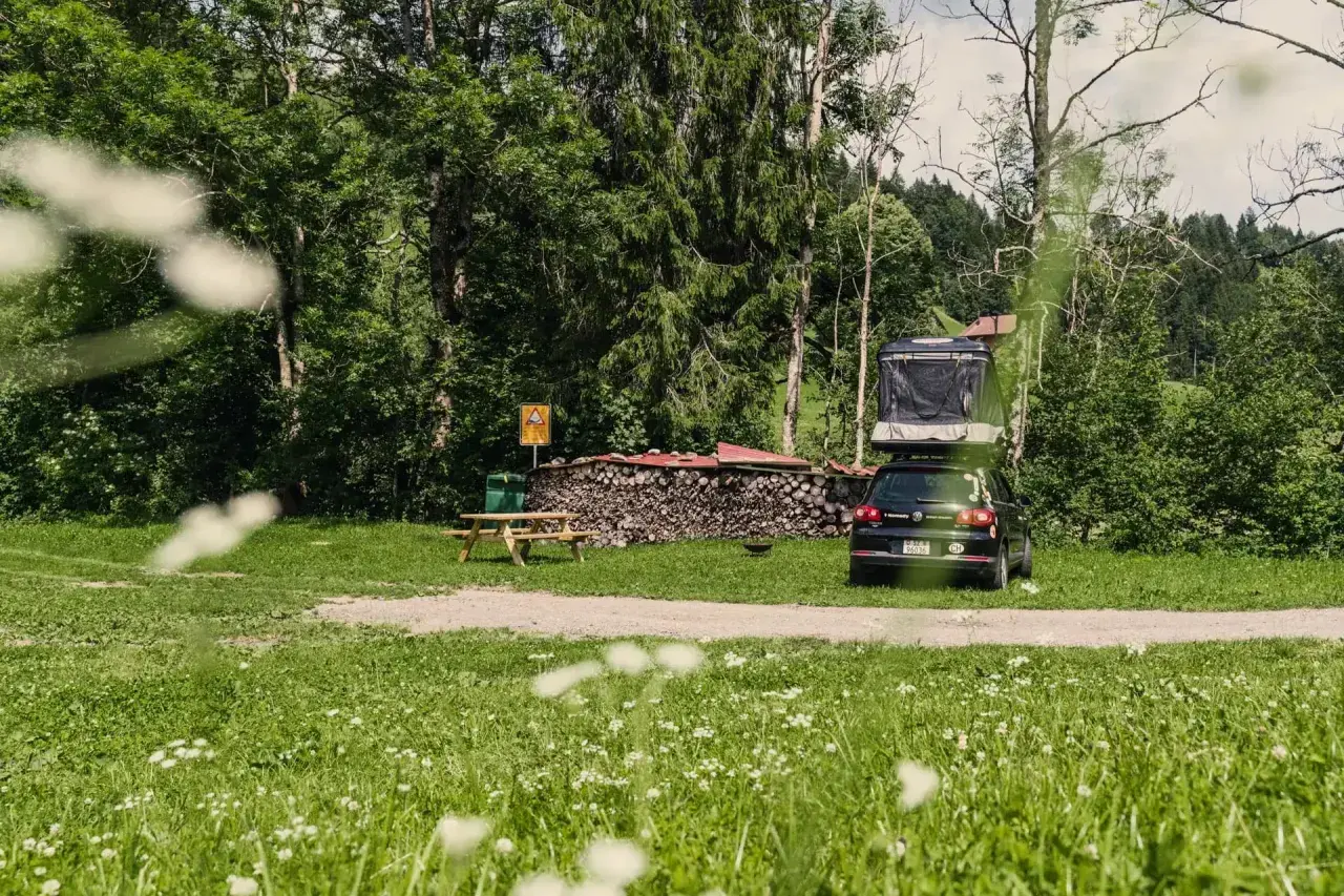 Campingplatz mit Dachzeltauto, Holzstapel und Picknicktisch. Ein idyllischer Ort für Basel Geheimtipps abseits des Trubels.