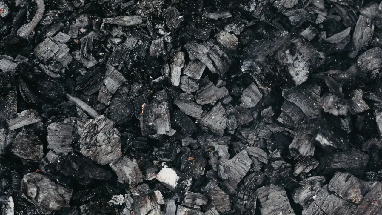 Gros plan sur des morceaux de machefer pellet, résidus noirs et gris de combustion, évoquant la chaleur d'un feu de bois.