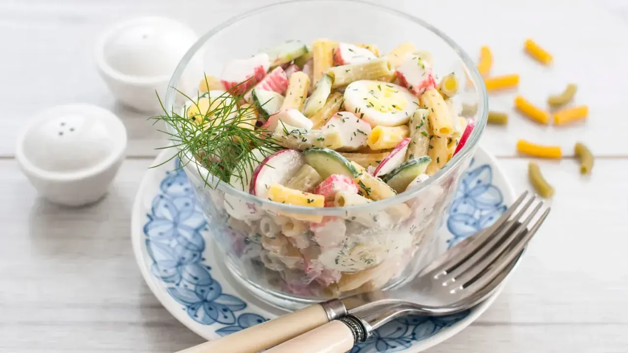 Salade de pâtes au surimi, œufs durs, concombre et radis, garnie d'aneth. Un délice frais et coloré.