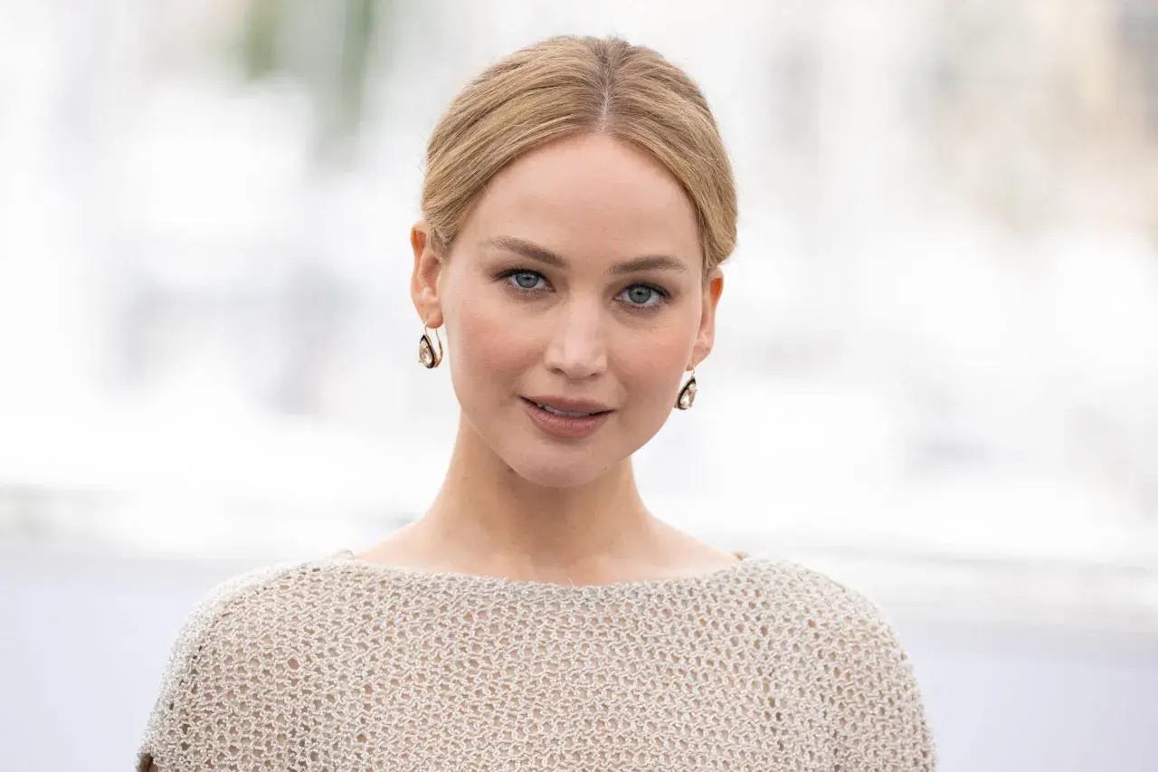Jennifer Lawrence, gwiazda wielu filmów, w beżowym swetrze i złotych kolczykach.