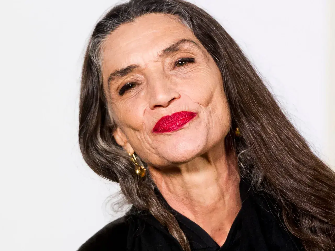 Mujer mayor con labios rojos vibrantes y cabello largo y oscuro. Un ejemplo de cómo maquillarse a los 60, resaltando la belleza madura.