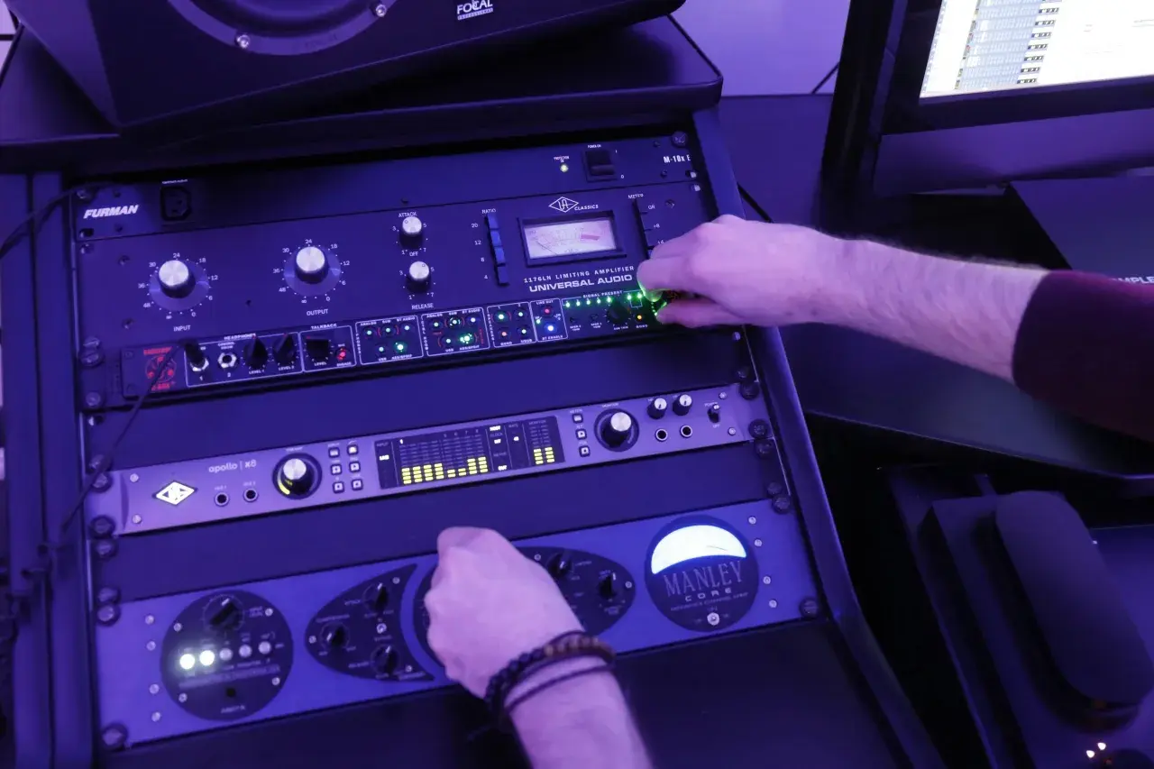 Main d'un ingénieur du son ajustant les potentiomètres d'un rack d'équipement audio, en pleine action de mastering musique.