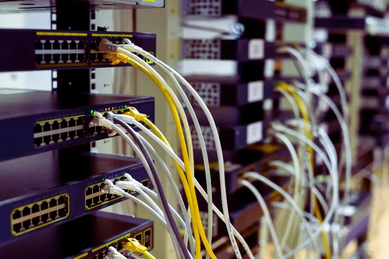 Faisceau de câblage RJ45 b, avec des câbles blancs, jaunes et gris connectés à des commutateurs réseau empilés.