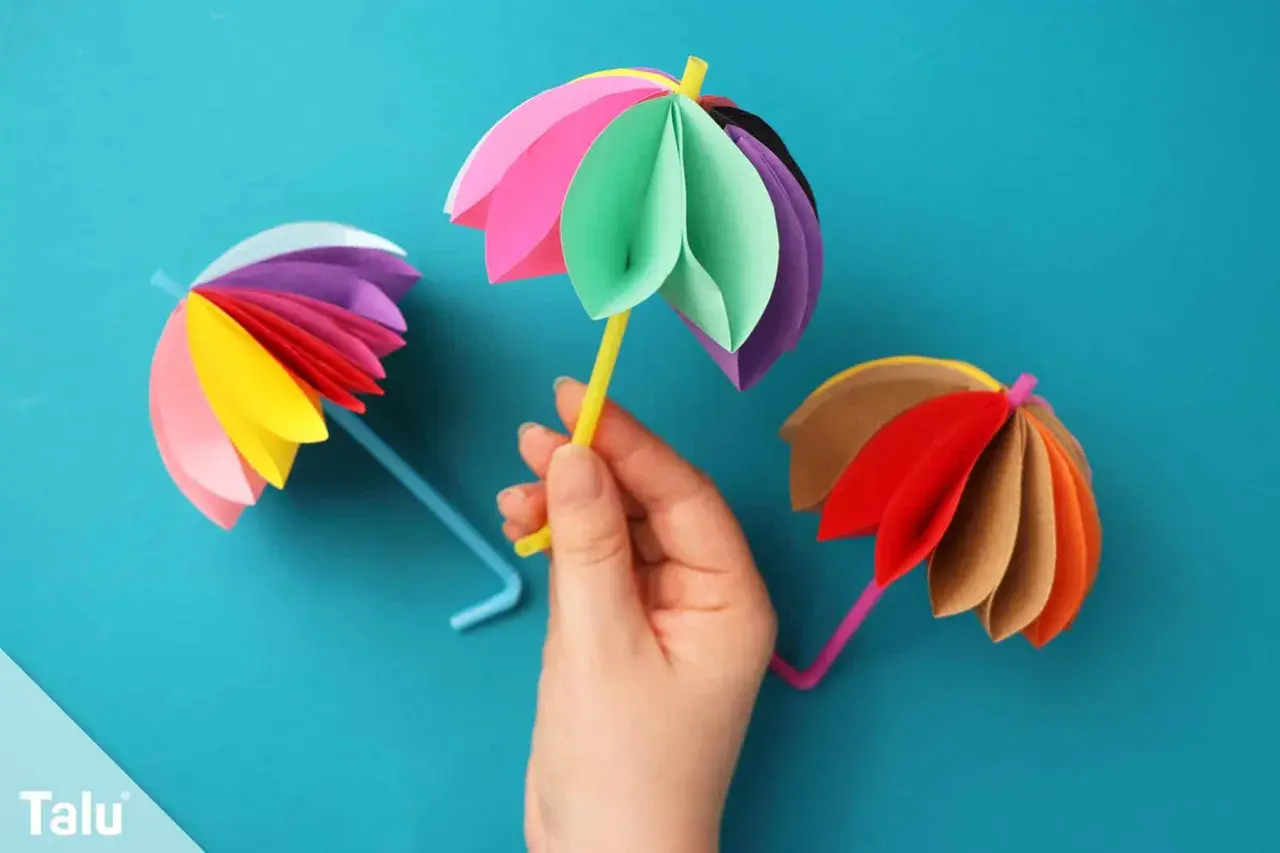 Bunte Papier-Regenschirme, die zum **Regenschirm basteln einfach** einladen. Ein gelber Strohhalm hält einen bunten Schirm.