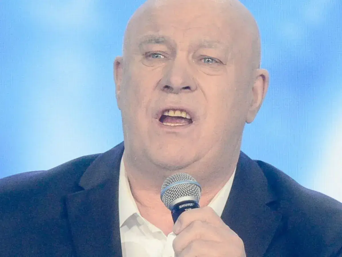 Ryszard Rynkowski śpiewa, trzymając mikrofon. Jego charakterystyczne utwory poruszają serca słuchaczy.