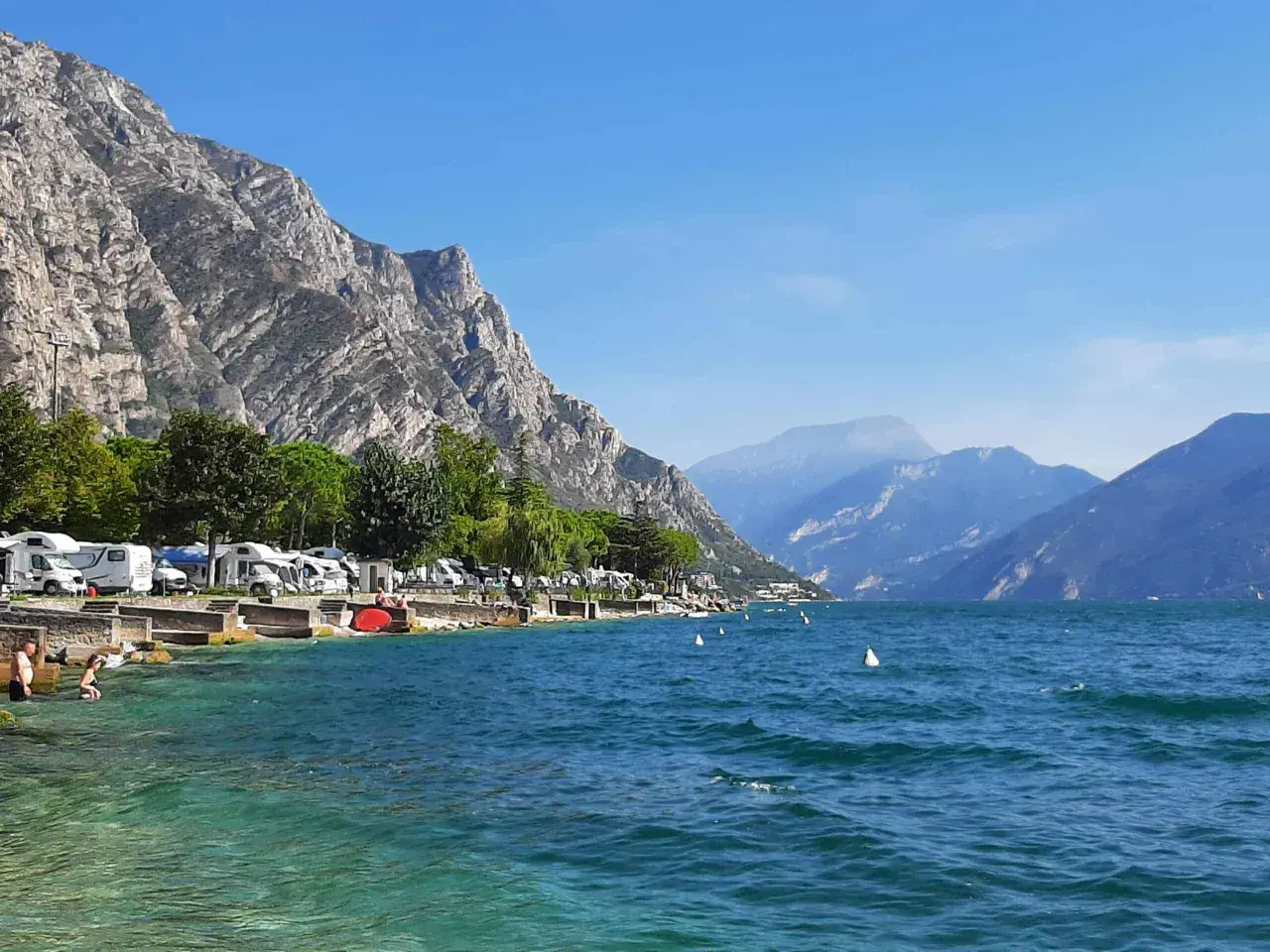 Malowniczy widok na jezioro Garda z campingiem, kamienistym brzegiem i górami w tle. Idealne miejsce na wakacje.