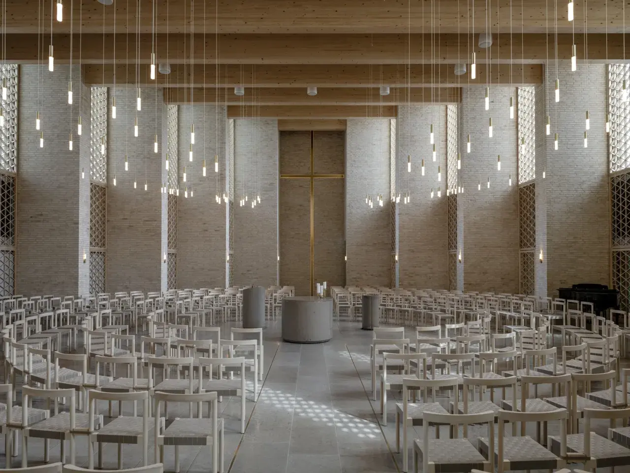 Innenraum einer modernen Kirche mit Reihen von Holzbänken, einem goldenen Kreuz und vielen hängenden Lichtern.