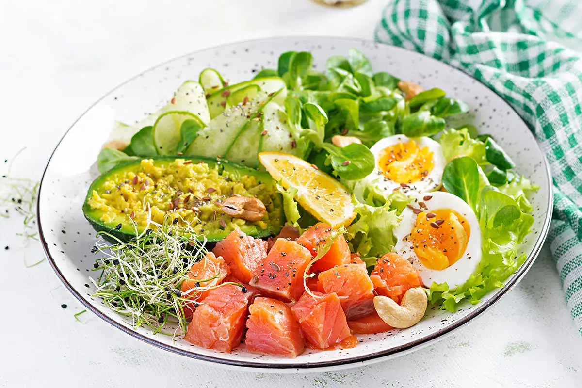 Un'idea per cosa mangiare a pranzo: un piatto colorato con salmone a cubetti, avocado, uova sode, cetrioli e germogli.