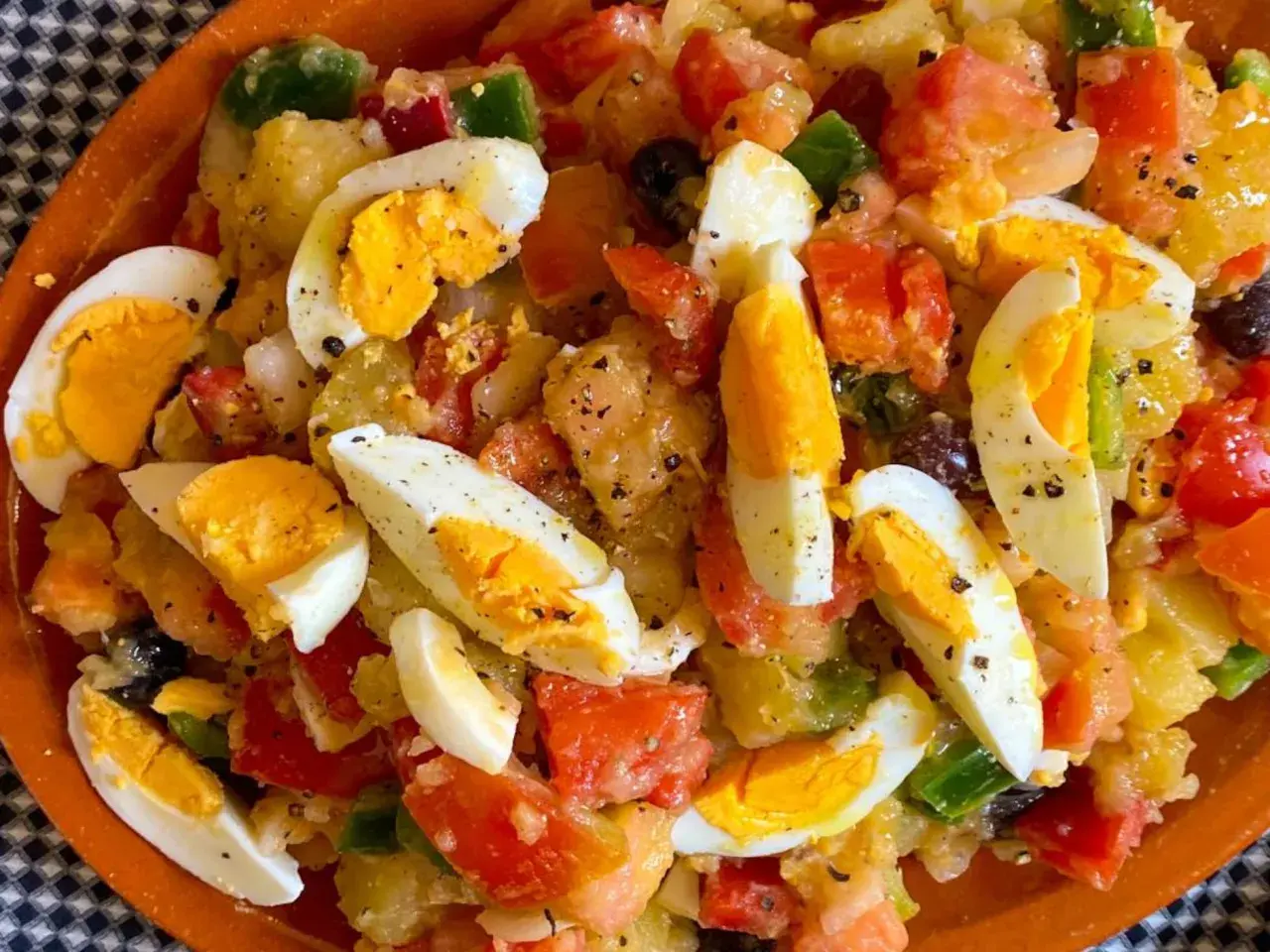 Ensalada campera con patatas, huevos duros, tomate, pimiento y aceitunas negras, todo mezclado y sazonado.