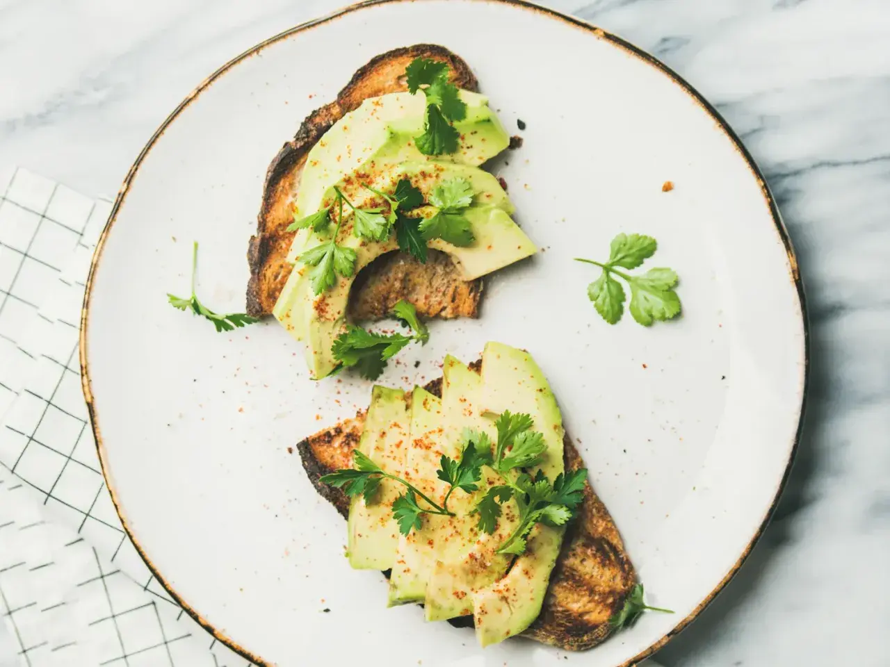 Deux toasts avec avocat tranché, persil frais et une pincée d'épices. Un avocat avec quoi, un délice simple et sain.