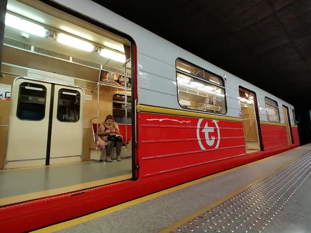 Kobieta czeka na swiateczne metro. Czerwony wagon z białym logo.