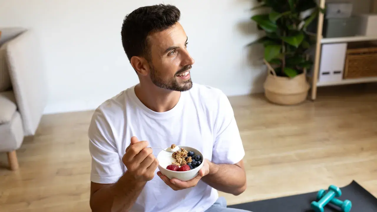Un jeune intermittent savoure un bol de yaourt grec avec des fruits rouges et du granola, prêt pour sa journée.