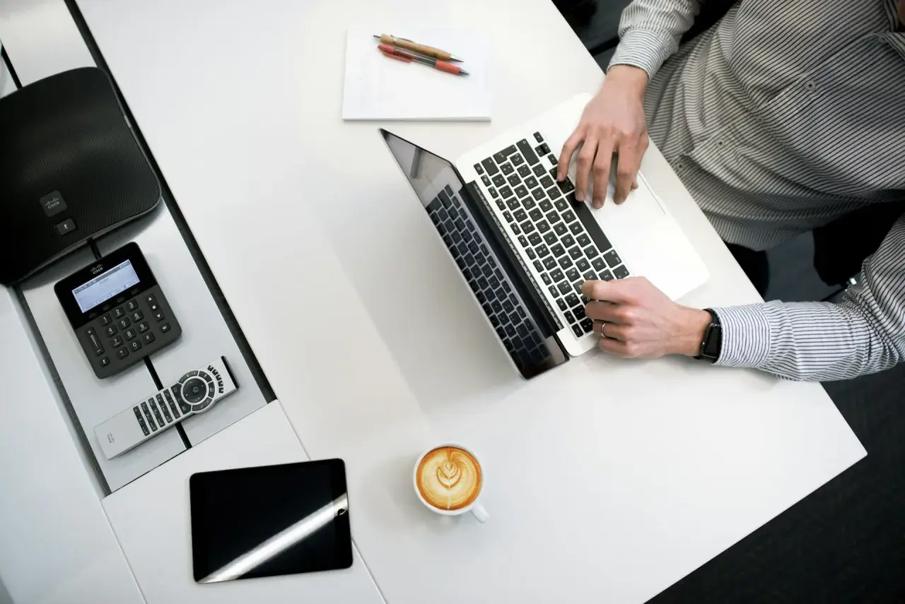 Kto to jest administrator? To osoba pracująca przy laptopie, z telefonem Cisco, tabletem i kawą.
