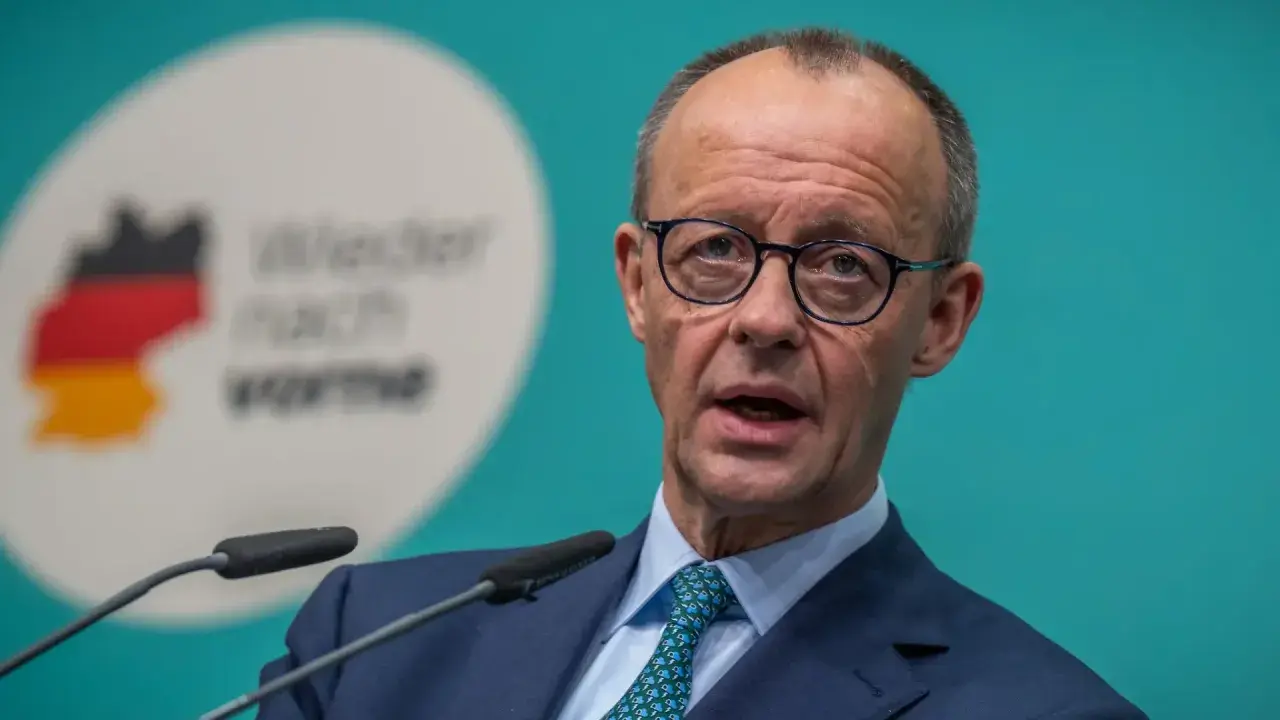 Mann mit Brille spricht ins Mikrofon. Im Hintergrund eine Deutschlandkarte mit Flaggenfarben und der Aufschrift "Wieder nach vorne". Möglicherweise im Kontext einer rtl aktuell umfrage.