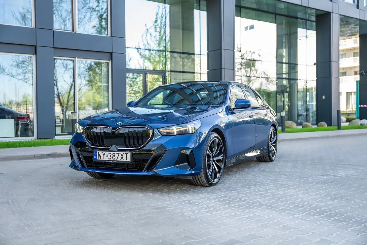 Eleganckie, granatowe BMW 540d z nowoczesnym designem, zaparkowane przed szklanym budynkiem.