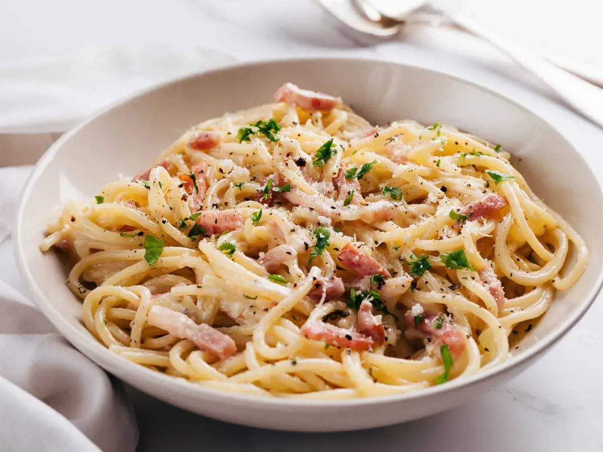 Un plat de pâtes à la carbonara crémeuses, garni de lardons, de parmesan râpé et de persil frais. Un délice italien.