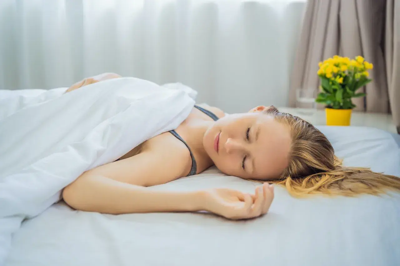 A woman sleeps peacefully on a white bed, her head resting directly on the mattress. Is it better to sleep without a pillow?
