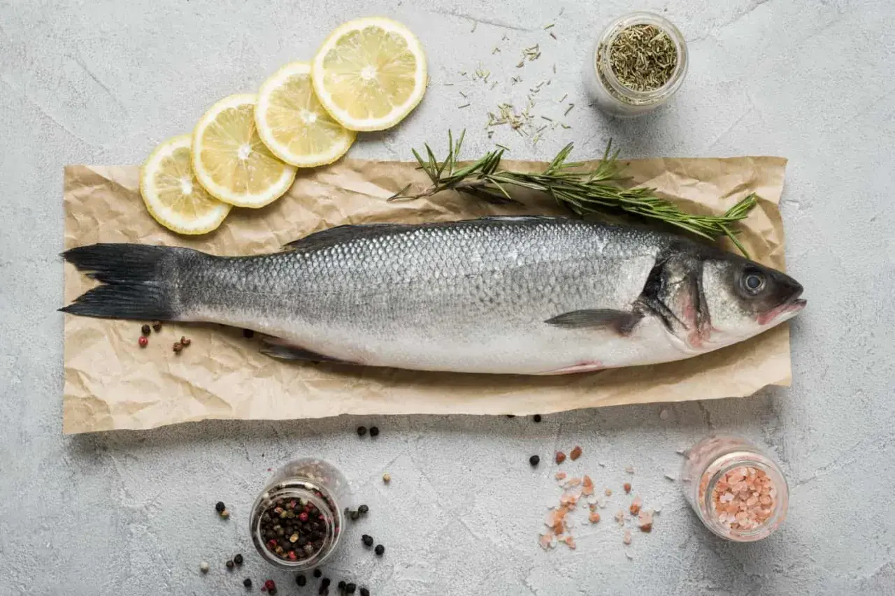 Lubina fresca, lista para cocinar. Un manjar de los pescados de temporada Galicia, acompañada de limón, romero y especias.