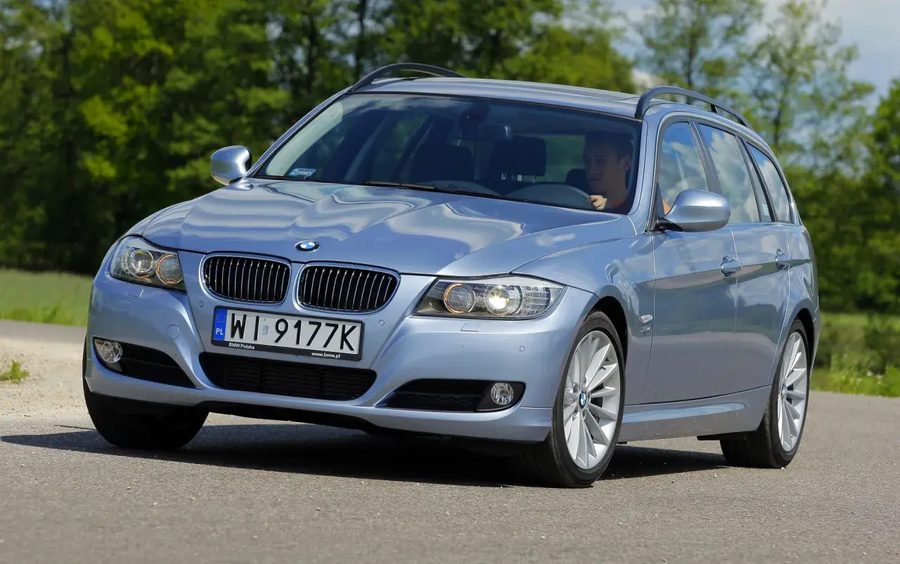 Błękitne BMW E91 na drodze, widać wyraźnie jego przednie światła i grill.