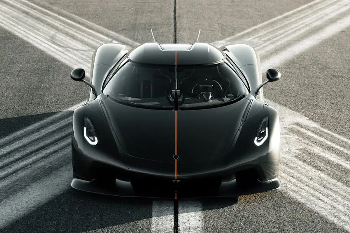 Czarny Koenigsegg Jesko z pomarańczowym pasem na masce, gotowy do startu na torze.