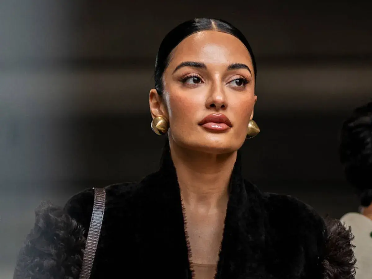 Mujer con peinado pulido y maquillaje natural, luciendo aretes dorados y un abrigo negro de pelo. Su **clean look** irradia elegancia.