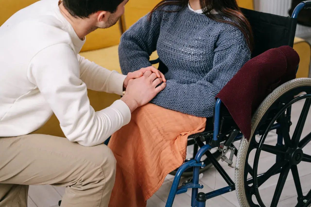 Uomo tiene la mano di una donna su sedia a rotelle, un gesto di supporto mentre si discute del pagamento invalidità civile.