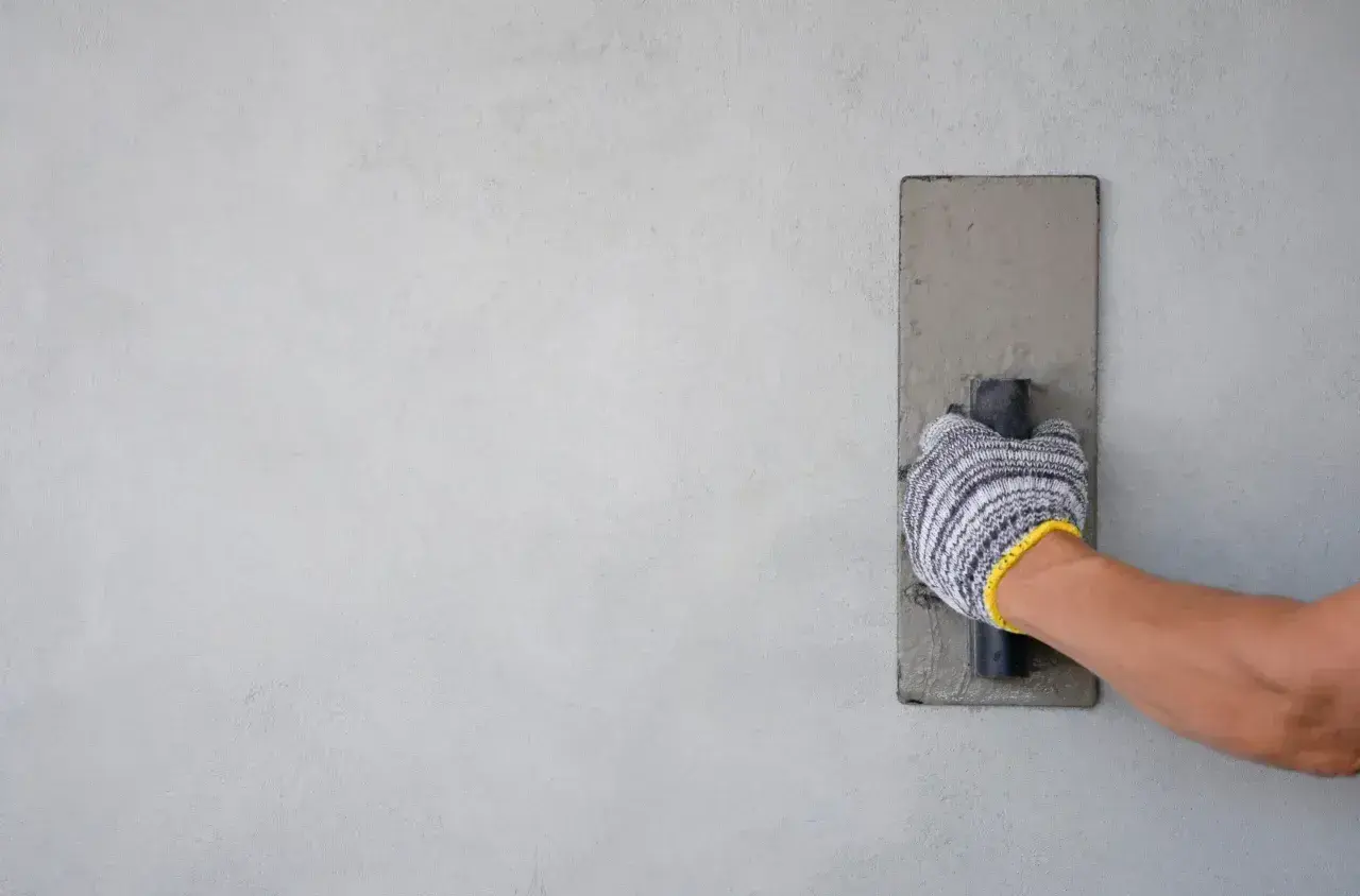 Mano con guanto che esegue la rasatura di un muro con una cazzuola.