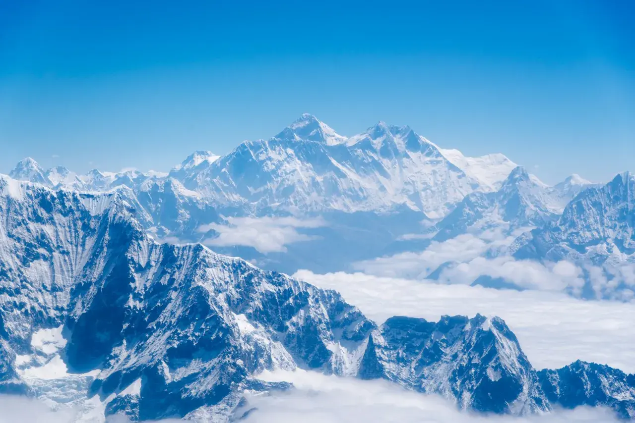 Majestatyczne, ośnieżone szczyty Himalajów, gdzie leży Mount Everest, wyłaniają się z morza chmur pod błękitnym niebem.
