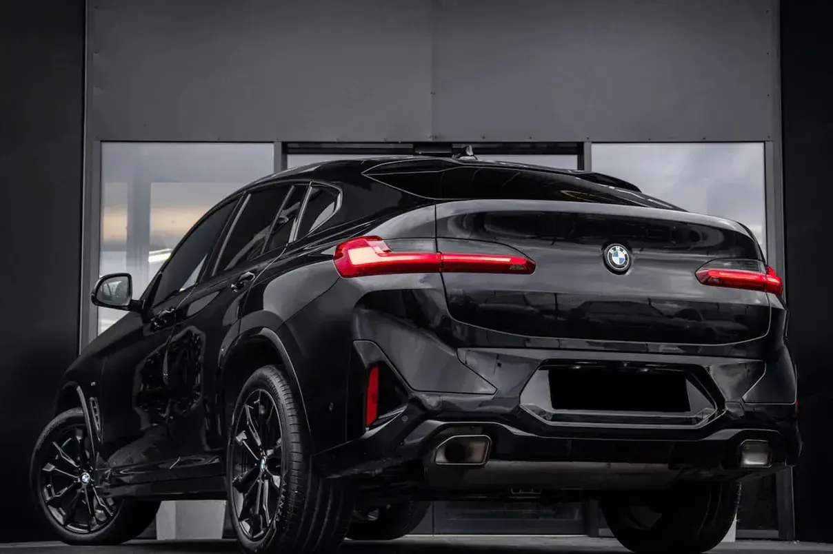 Elegancki, czarny BMW X4 G02 z przyciemnianymi szybami i sportowymi felgami prezentuje się imponująco na tle nowoczesnej, szarej ściany.