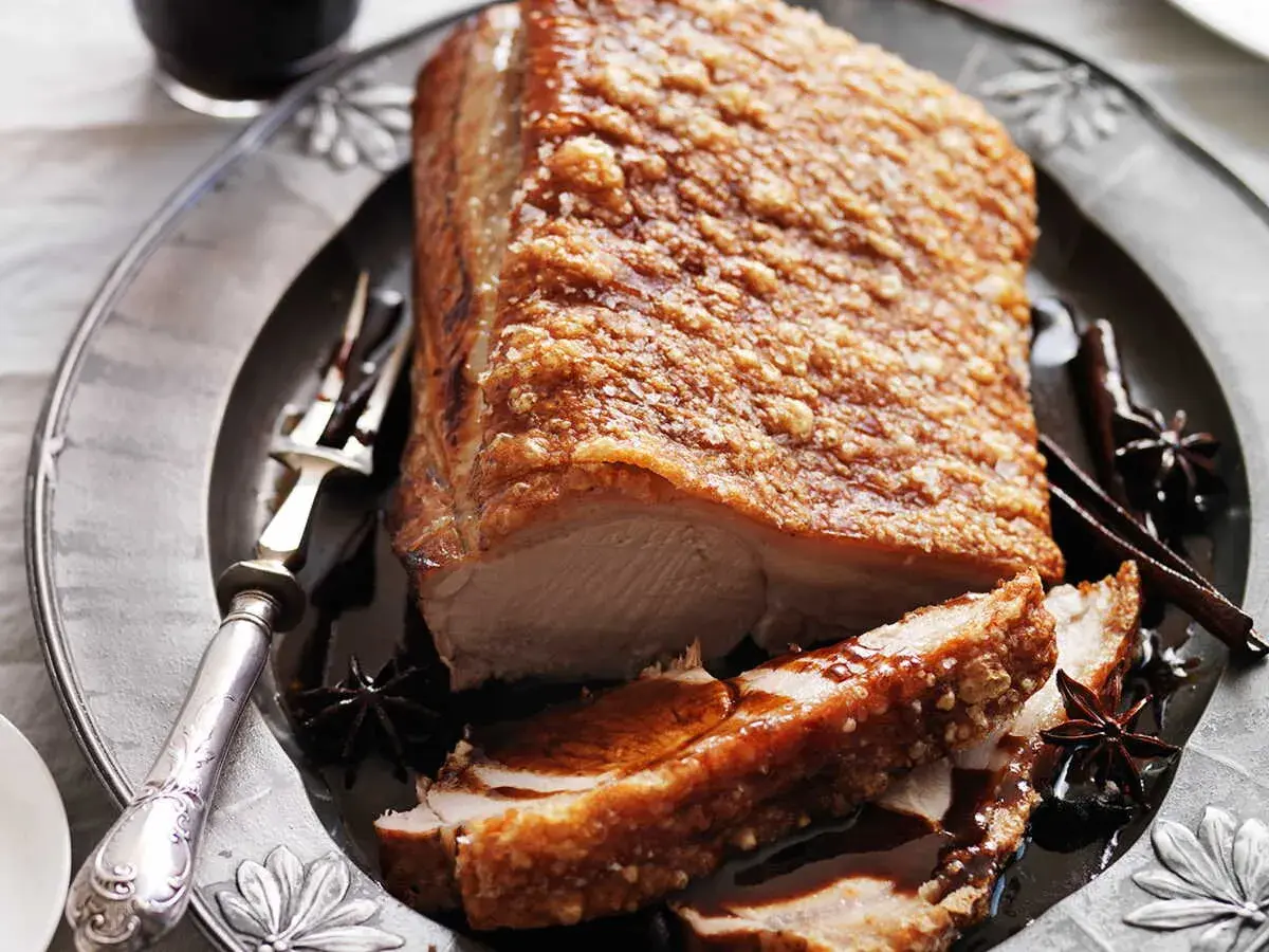 Poitrine de porc croustillante, dorée et juteuse, servie sur une assiette ornée avec des épices.