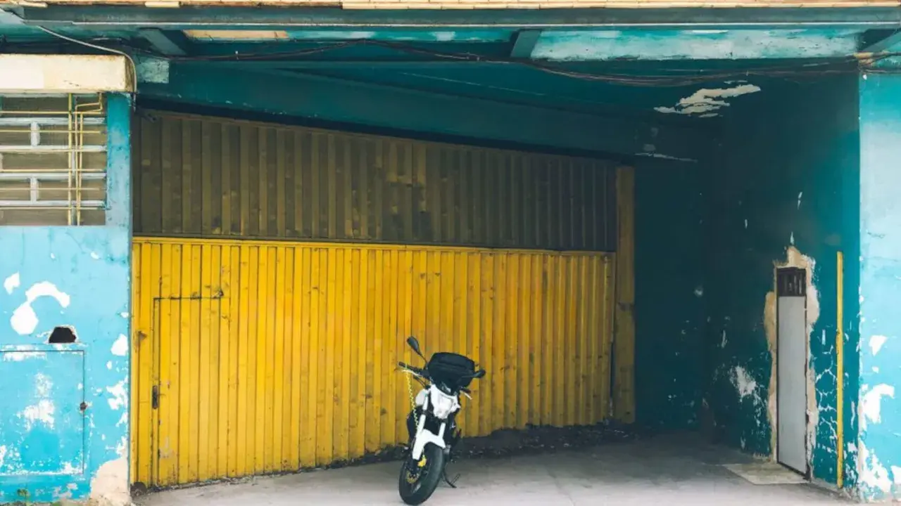 Moto aparcada frente a una cochera con puerta amarilla, se puede aparcar en una cochera sin vado.