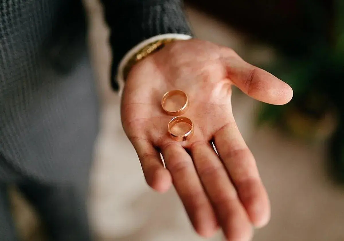 Dos anillos de oro descansan en una mano abierta, listos para ajustar el anillo y sellar un compromiso.