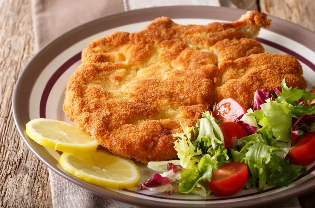 Chrupiący kotlet milanese z cytryną i świeżą sałatką z pomidorkami.