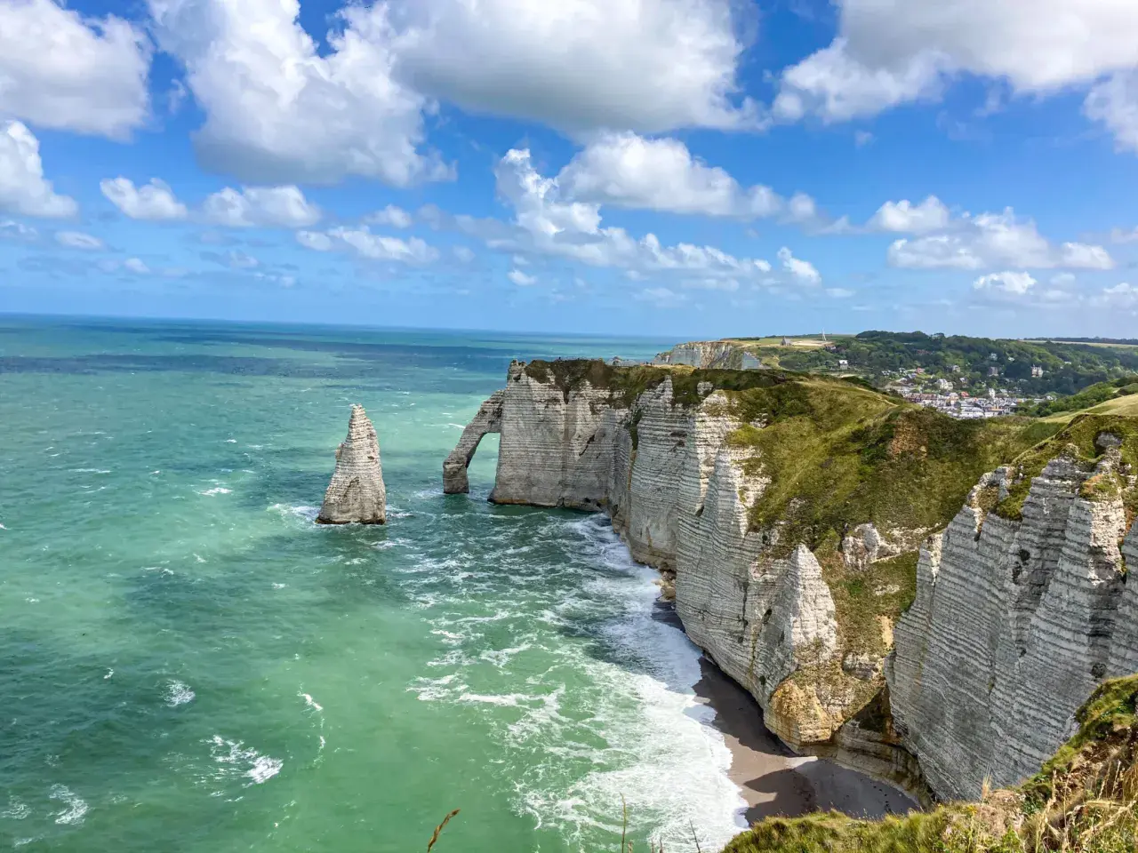 Klify w Étretat, Normandia: białe skały, łuk skalny i iglica w zielonym morzu.