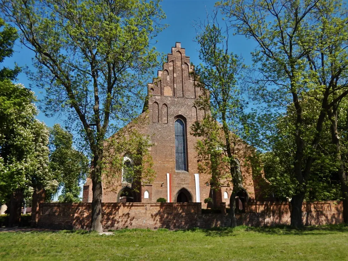 Gotycka ceglana świątynia, prawdopodobnie kościół pw. św. Jadwigi, otoczona zielenią. W tle błękitne niebo. Halszka Szamotuły.