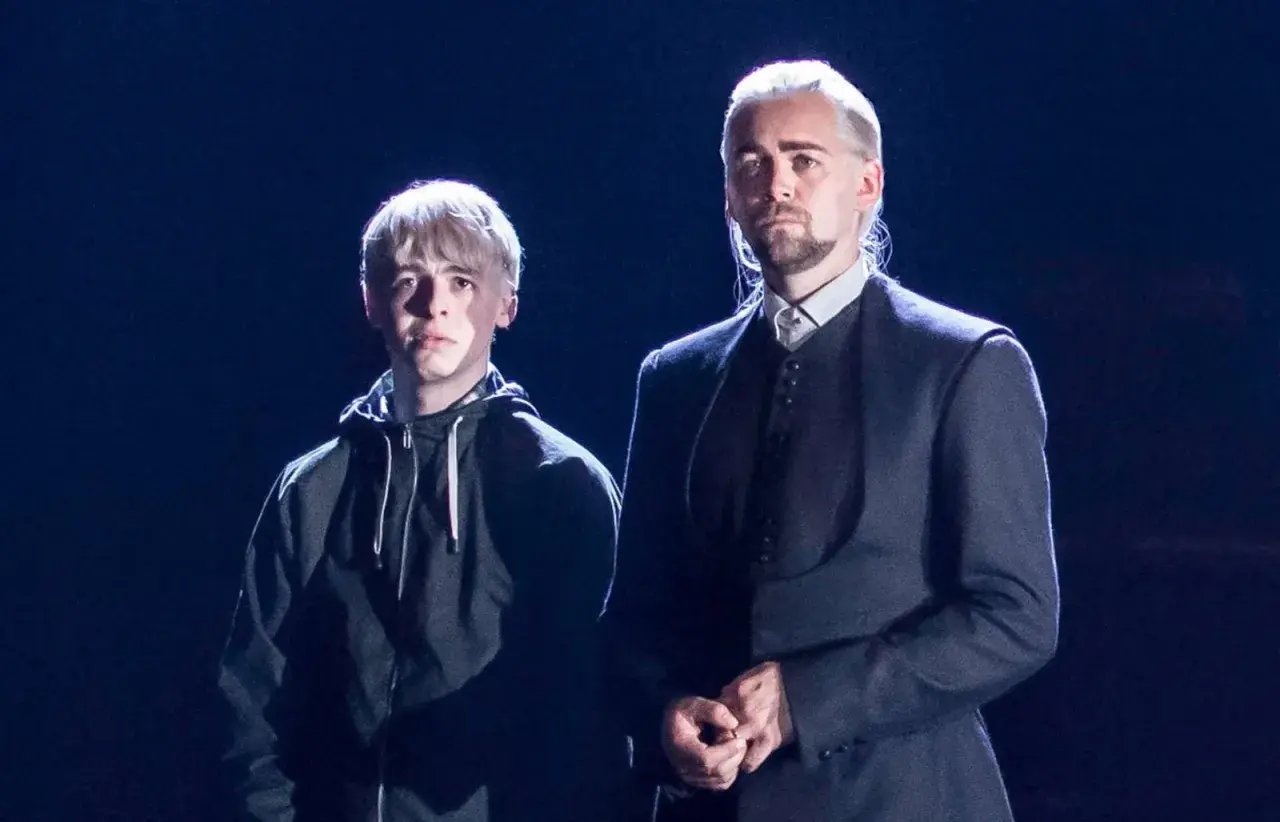 Scorpius Malfoy w czarnej bluzie obok starszego mężczyzny w eleganckim stroju.