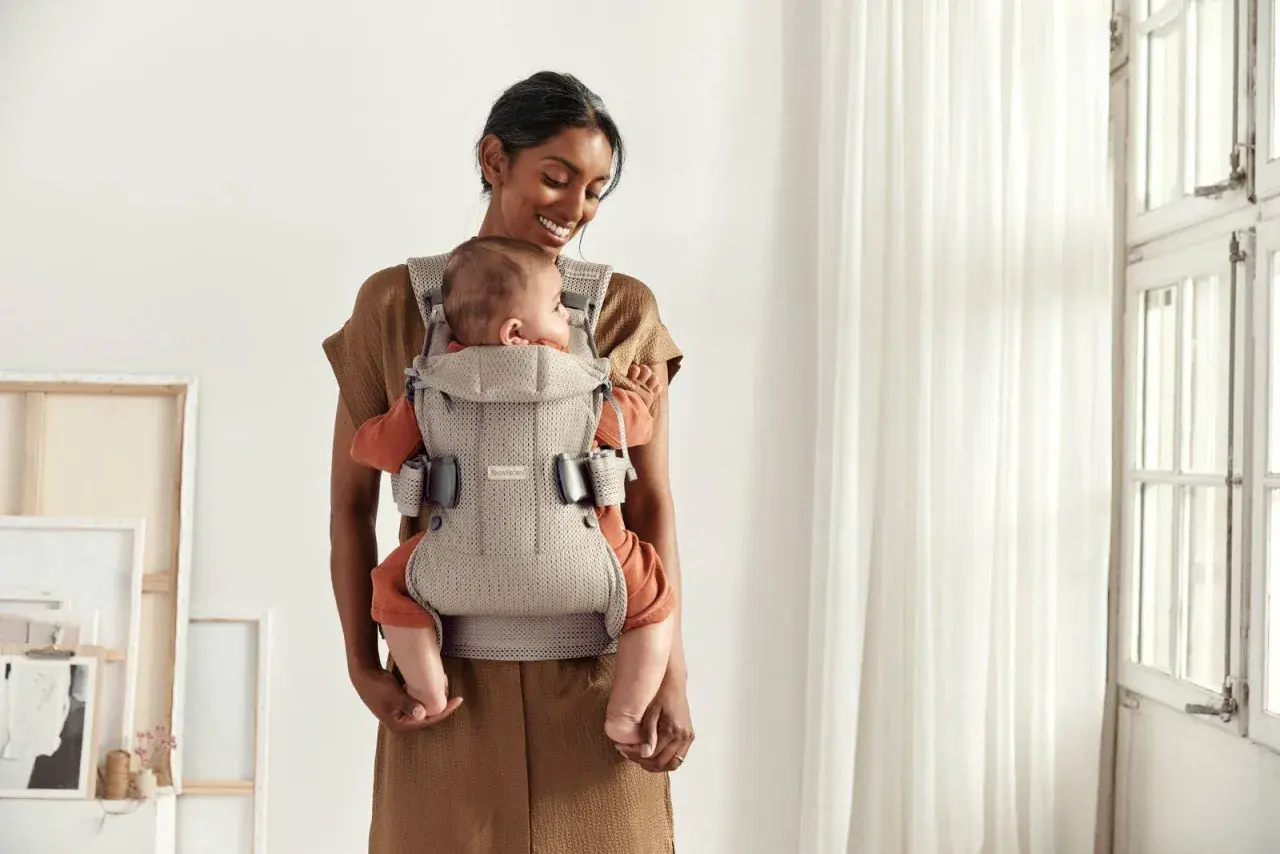 Uśmiechnięta mama tuli dziecko w nosidełku Babybjorn. Od kiedy można używać? Od pierwszych dni życia!