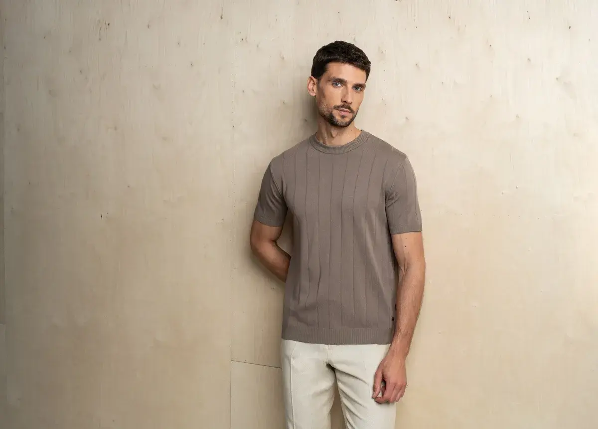 Mężczyzna prezentuje elegancki, casualowy styl. Brązowa, prążkowana koszulka z krótkim rękawem i beżowe spodnie tworzą harmonijną całość.