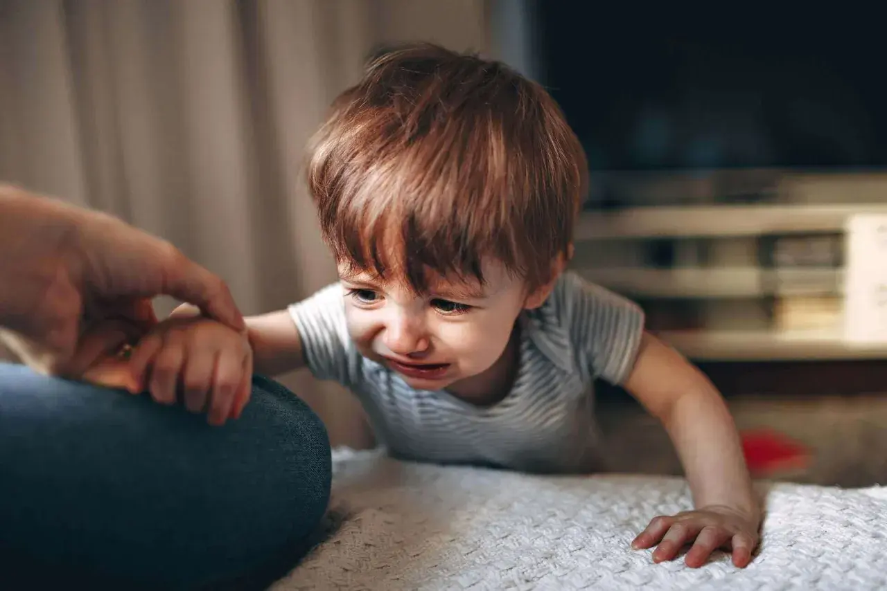 Gråtande bebis med rött hår, en high need baby som håller en vuxen hand.