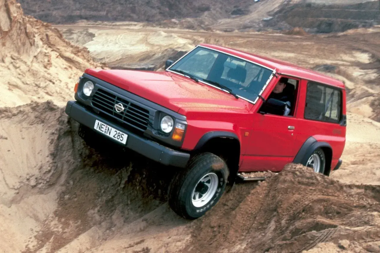 Czerwony Nissan Patrol Y60 pokonuje piaszczyste wzniesienie, demonstrując swoje terenowe możliwości.