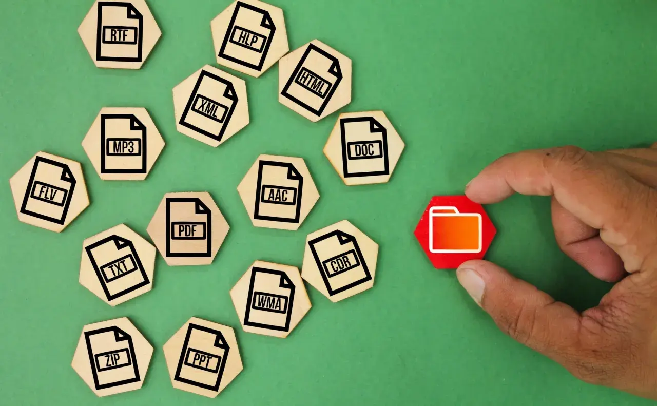 Un dedo toca una carpeta roja, rodeada de fichas de madera con extensiones de archivo como ZIP, MP3, DOC, etc. que representan un archivo comprimido.