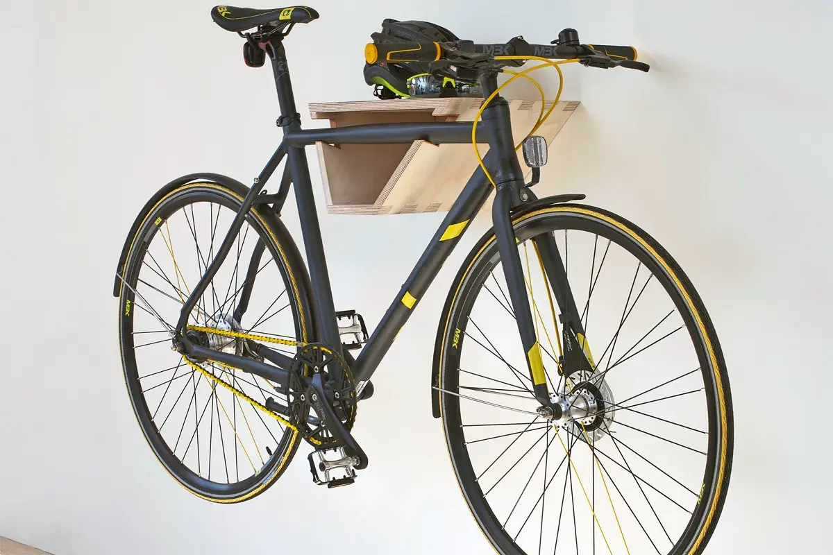 Schwarzes Fahrrad mit gelben Akzenten hängt an einer selbstgebauten Holz-Fahrrad-Wandhalterung. Helm liegt auf der Ablage.
