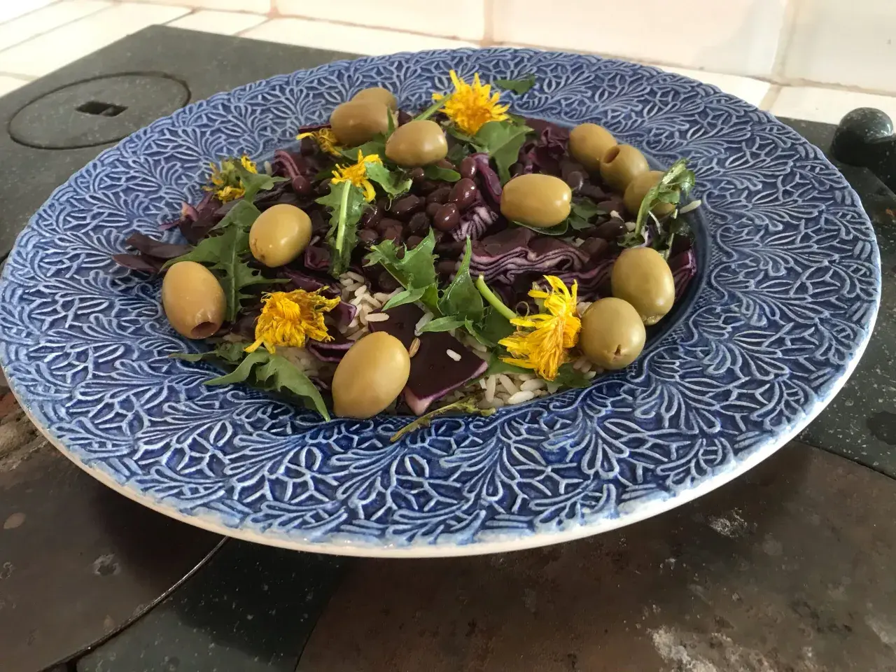 En blåmönstrad tallrik med en sallad av ris, svarta bönor, rödkål, oliver och maskrosblommor. Ett spännande maskros recept!