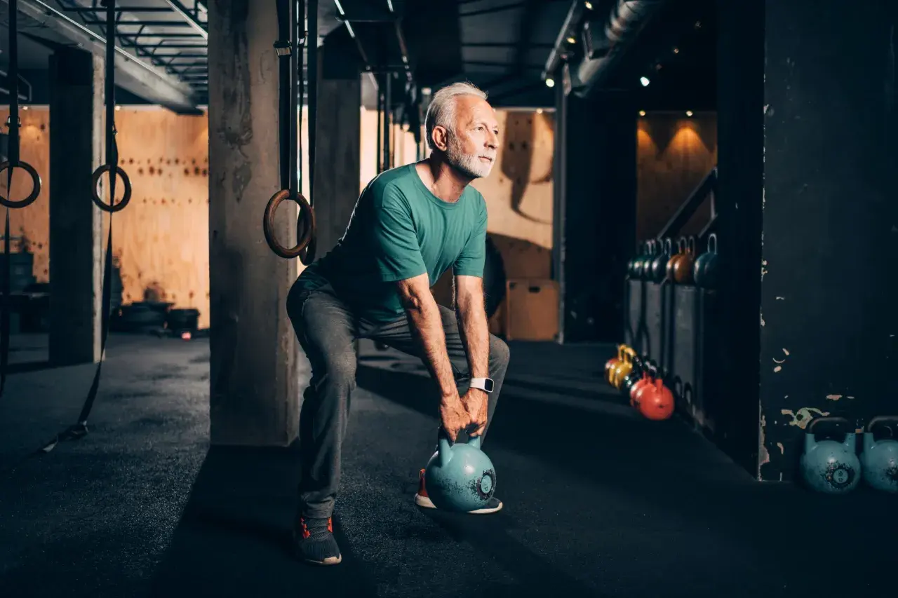 Älterer Mann trainiert mit Kettlebell, stärkt seine bauchmuskeln im Fitnessstudio.