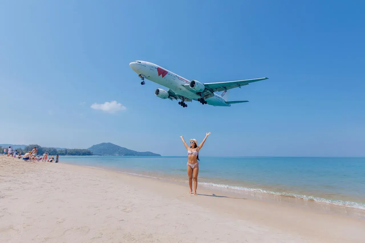 Frau am Strand jubelt, als ein Flugzeug landet. Der Traum vom Urlaub in Thailand wird mit dem Visum Thailand wahr.